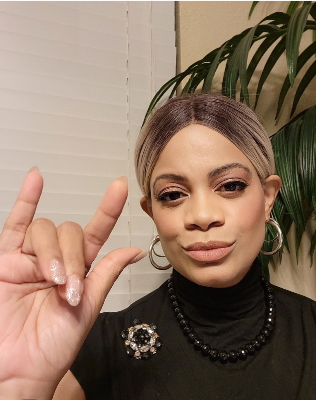 Angela Lynn in formal black attire making the ASL I love you sign.